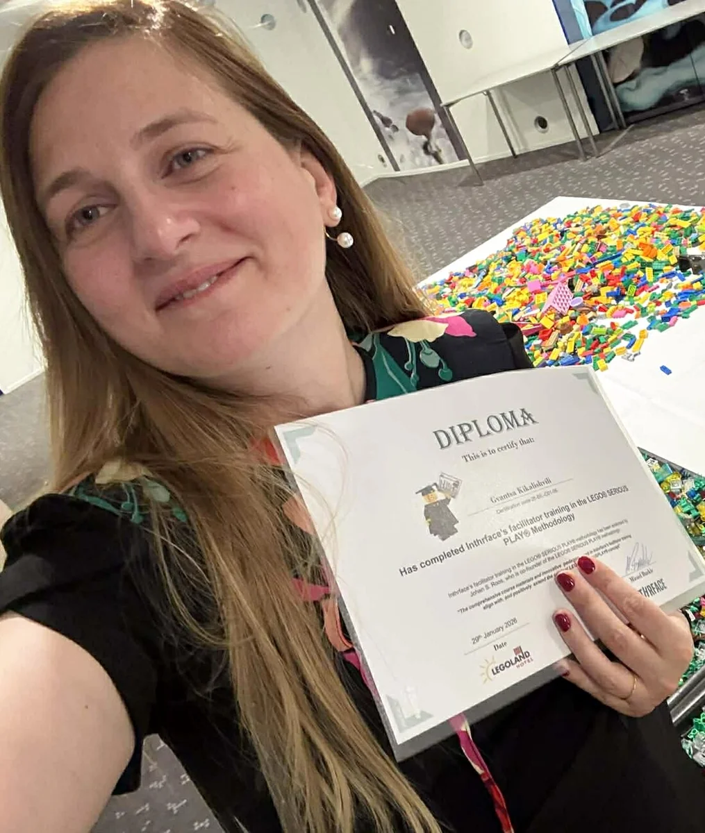 Gvantsa Kikalishvili holding her LEGO Serious Play facilitator certificate, with LEGO bricks in the background